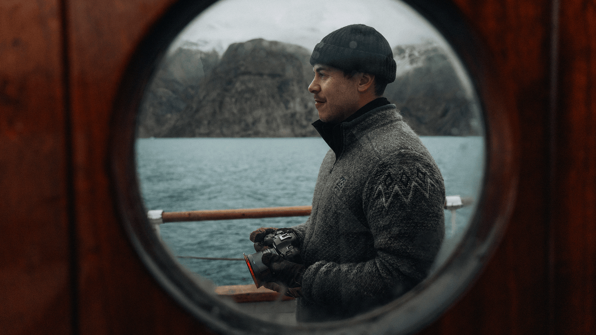 Fab Latham, Ambassador for Vallerret Photography GLoves, on a old sailboat in Greenland, with a costline in the background.